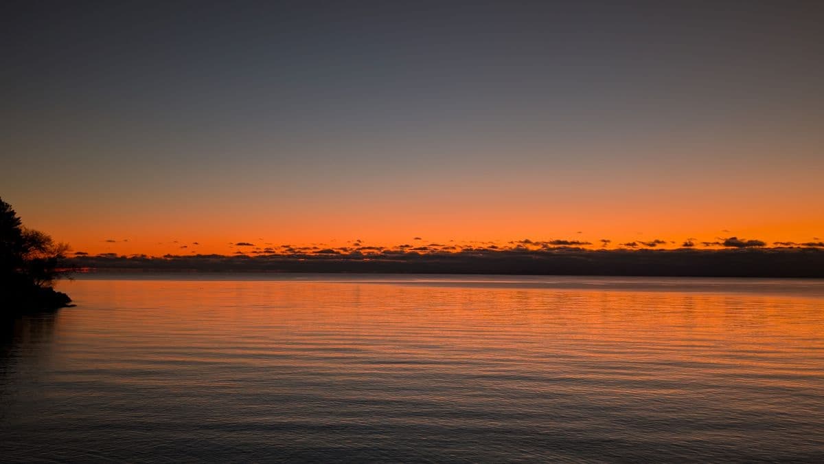 Photo of a Lake in Cowichan Valley at sunrise on a clear morning. The mountains and trees reflect off the calm water of the lake producing an image that looks like a sound waveform.